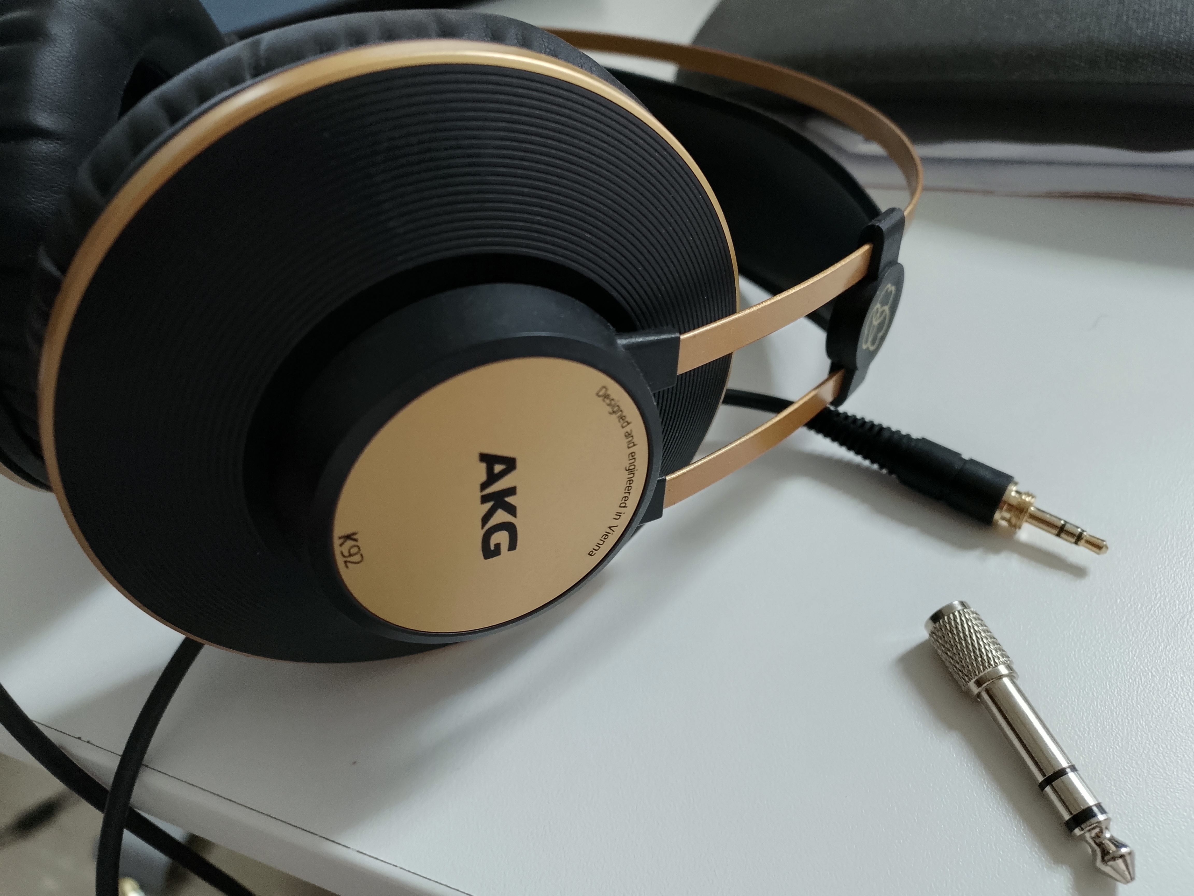 A close-up image of one cone of a pair of AKG K92 headphones, with the 1/8" cable visible as well as an adapter that adapts the 1/8" plug to fit in 1/4" sockets